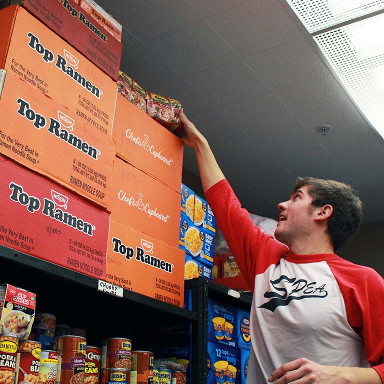 A SPEA student reaches for Ramen noodles as he helps stock a food bank.