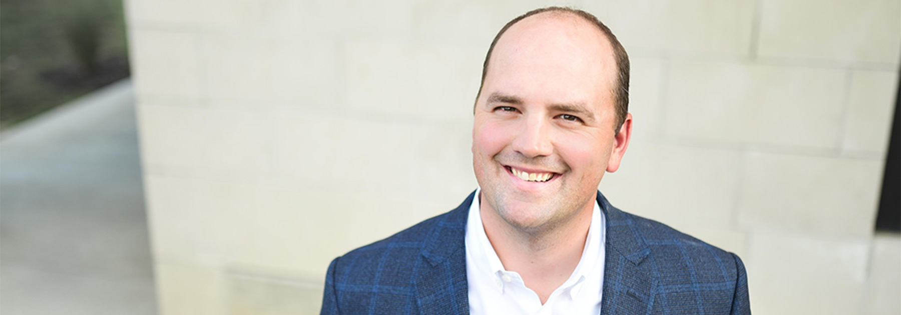 A man in a blue suit stands looking up and smiling.