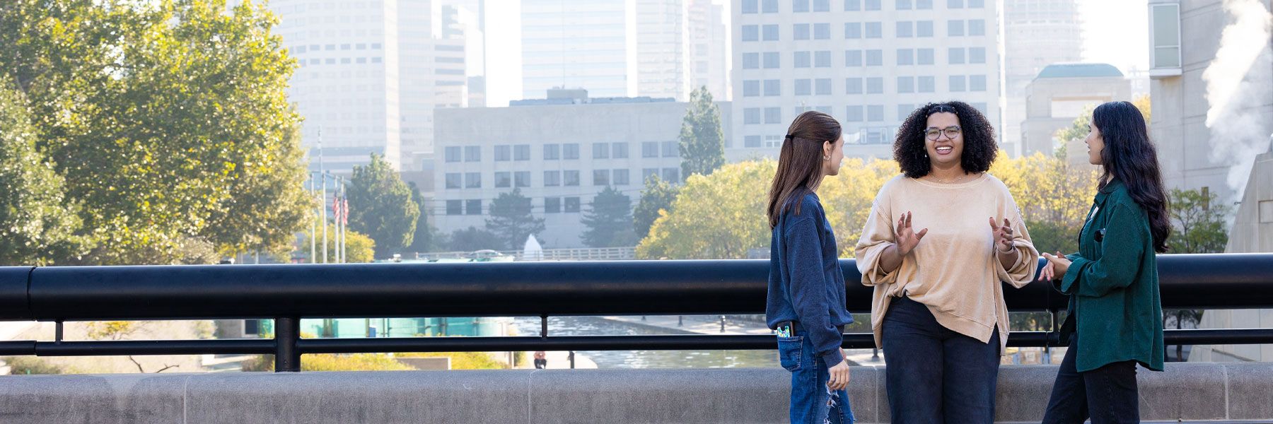 three students talking to each other in front of Indianapolis skyline