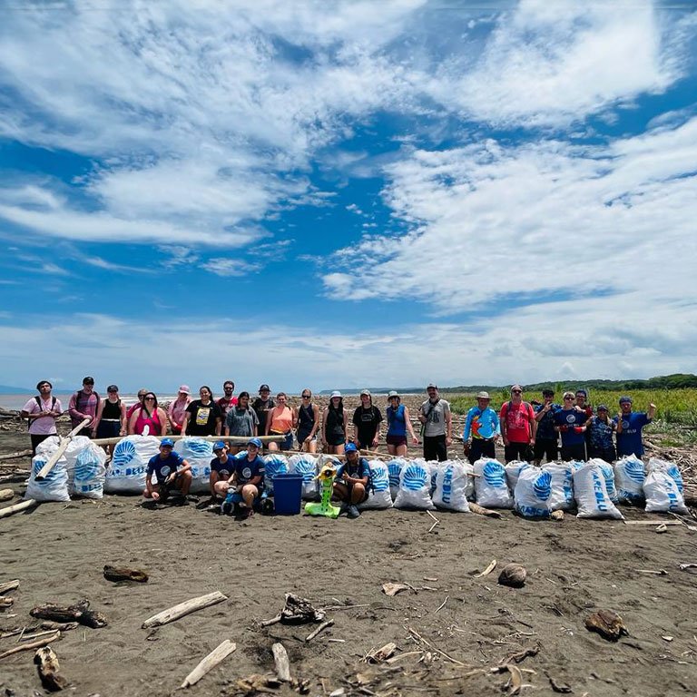 Students on a beach posing for a photo with bags of trash that they collected.